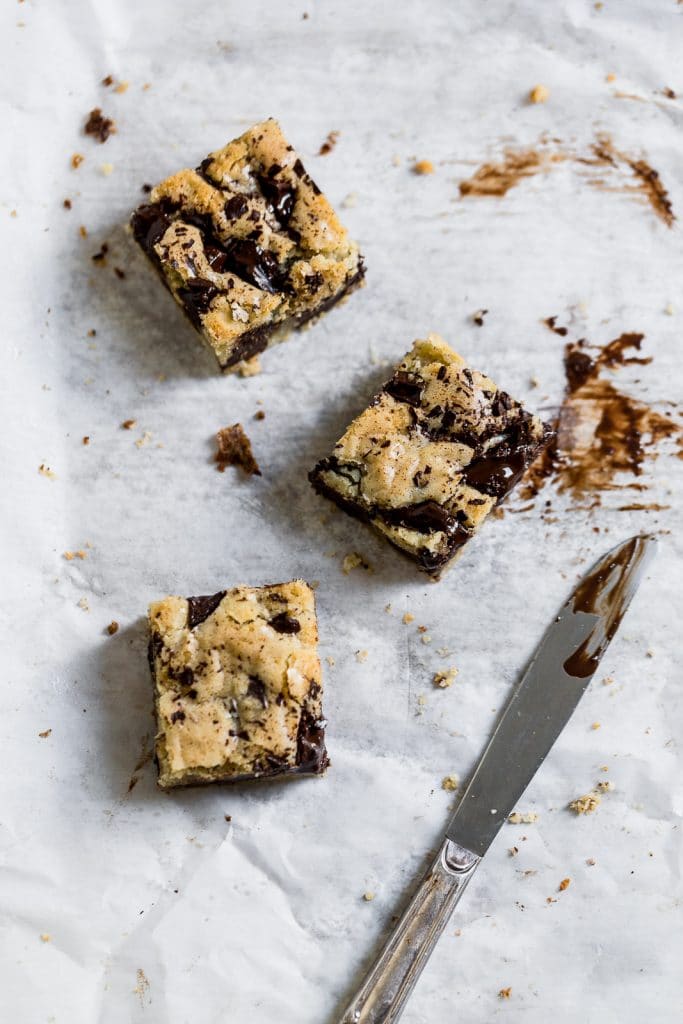 3 chocolate chip blondies arranged with a knife on a white surface