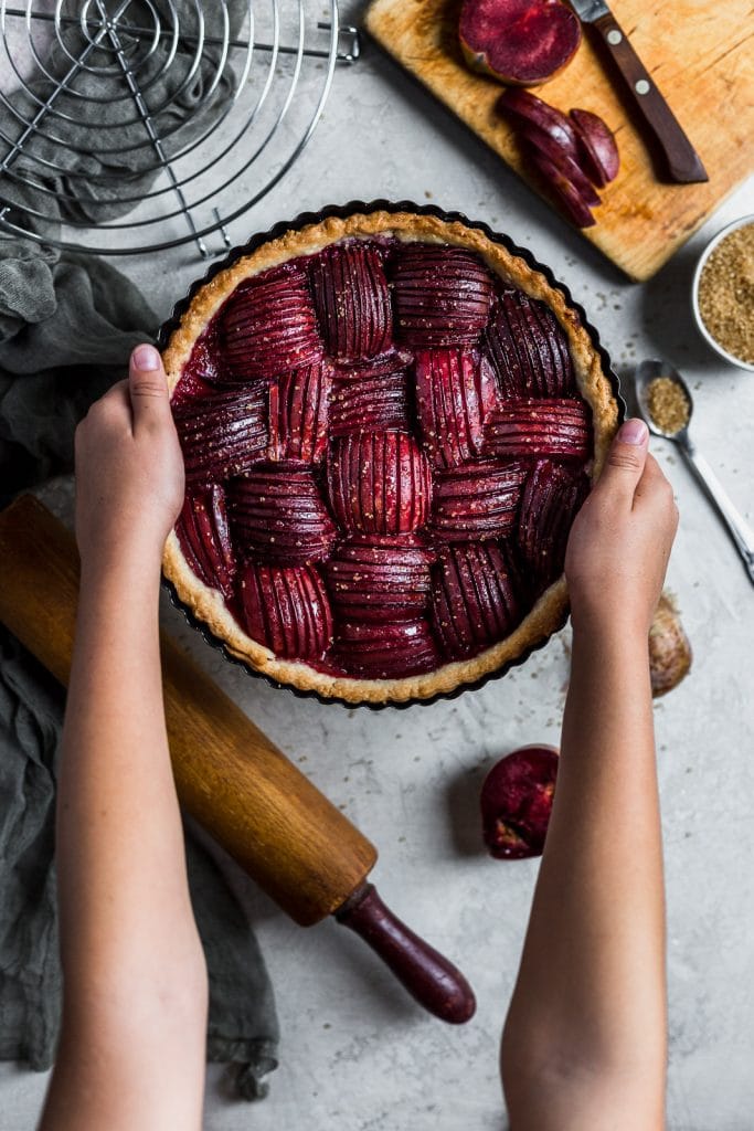 A child holding a plum tart with outstretched arms