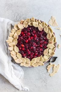 A pre-baked cranberry pie with leaf shapes made from a cookie cutter decorating the border of the pie.