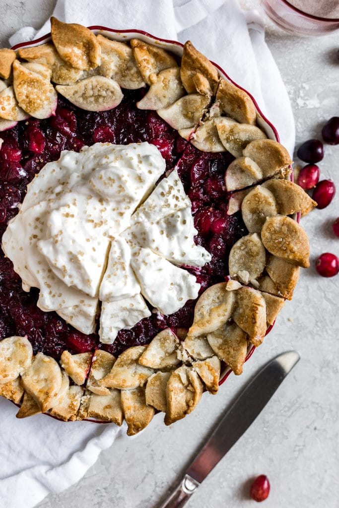 A closeup of a cranberry pie topped with whipped cream that has slices cut into it.