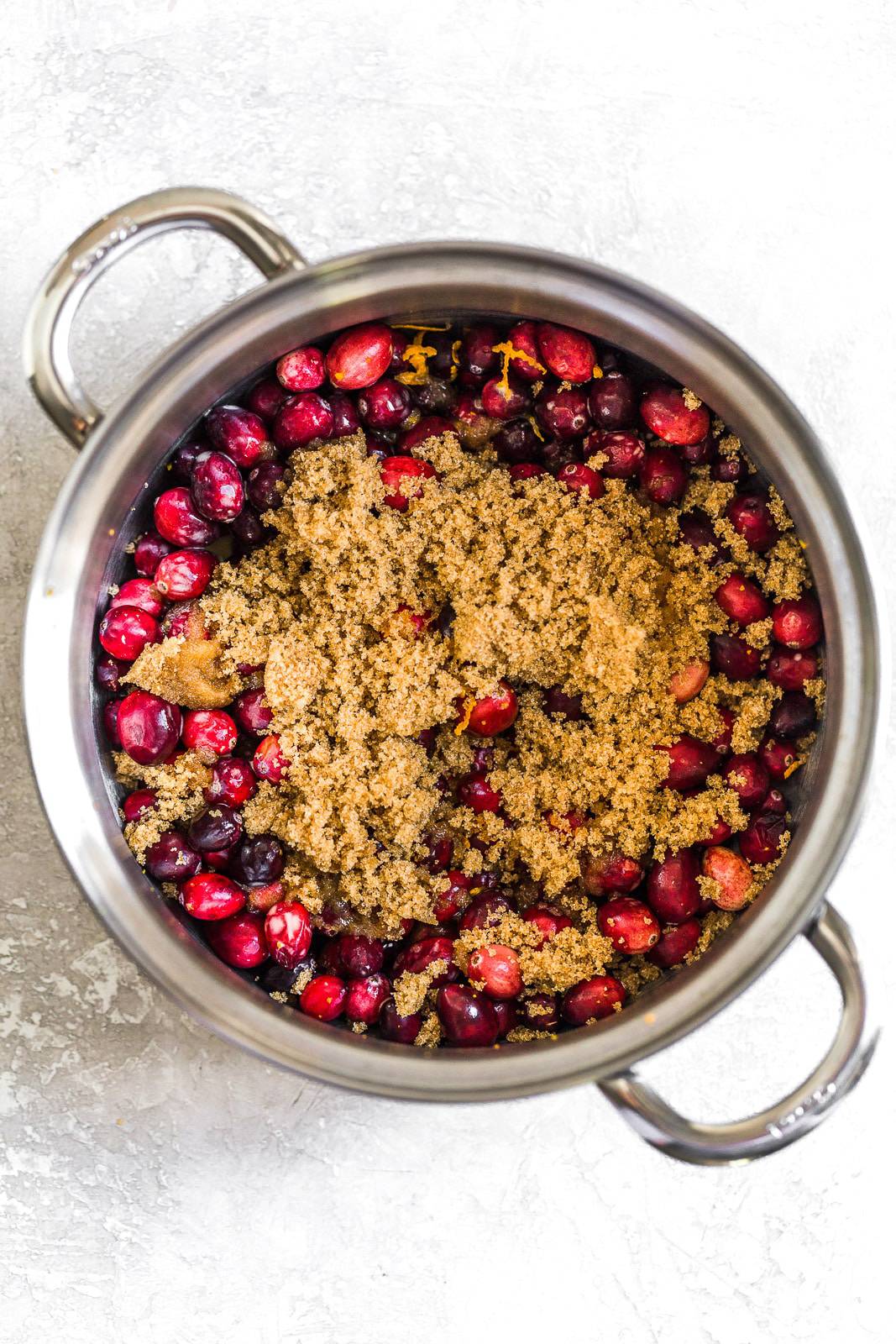Fresh cranberries, orange zest, and brown sugar mixed together in a pot.