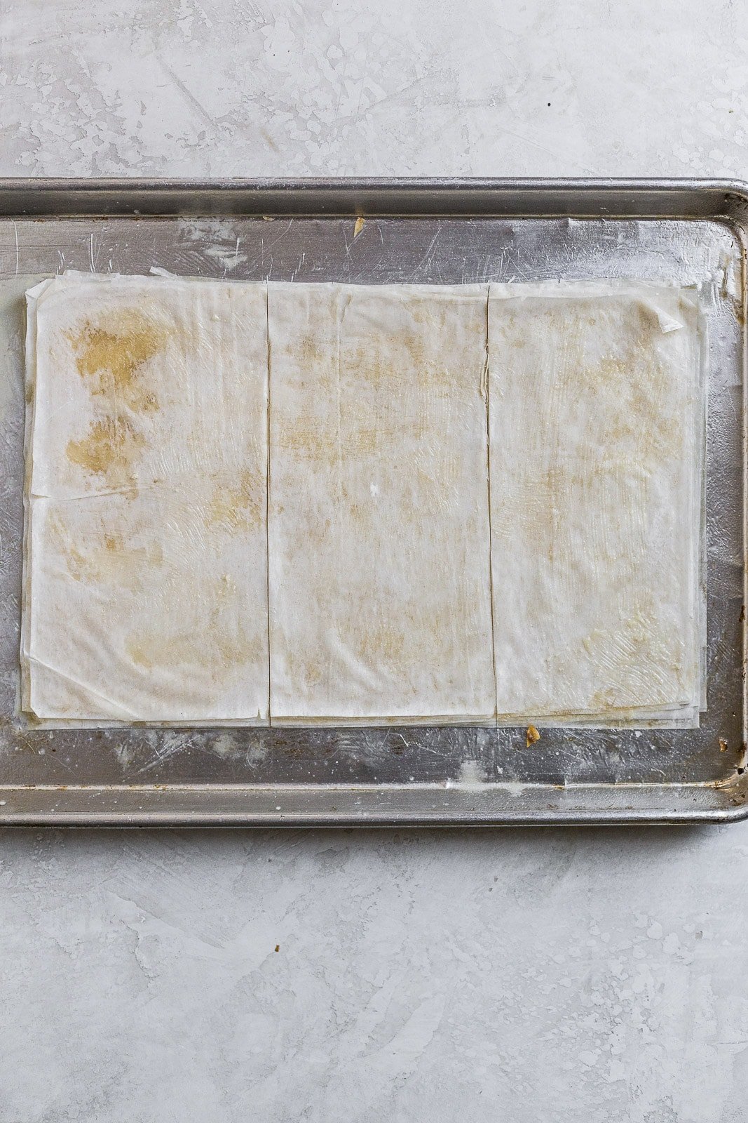 Phyllo dough layers brushed with butter and cut into thirds on a baking tray.