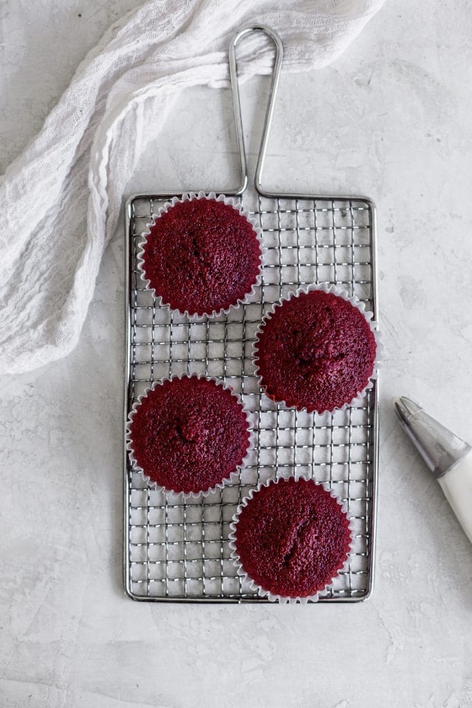 4 red velvet cupcakes infested sitting on a small wire rack on a gray background,