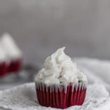 one red velvet cupcake with creamcheese frosting piped on top sitting on white cheesecloth on a gray background