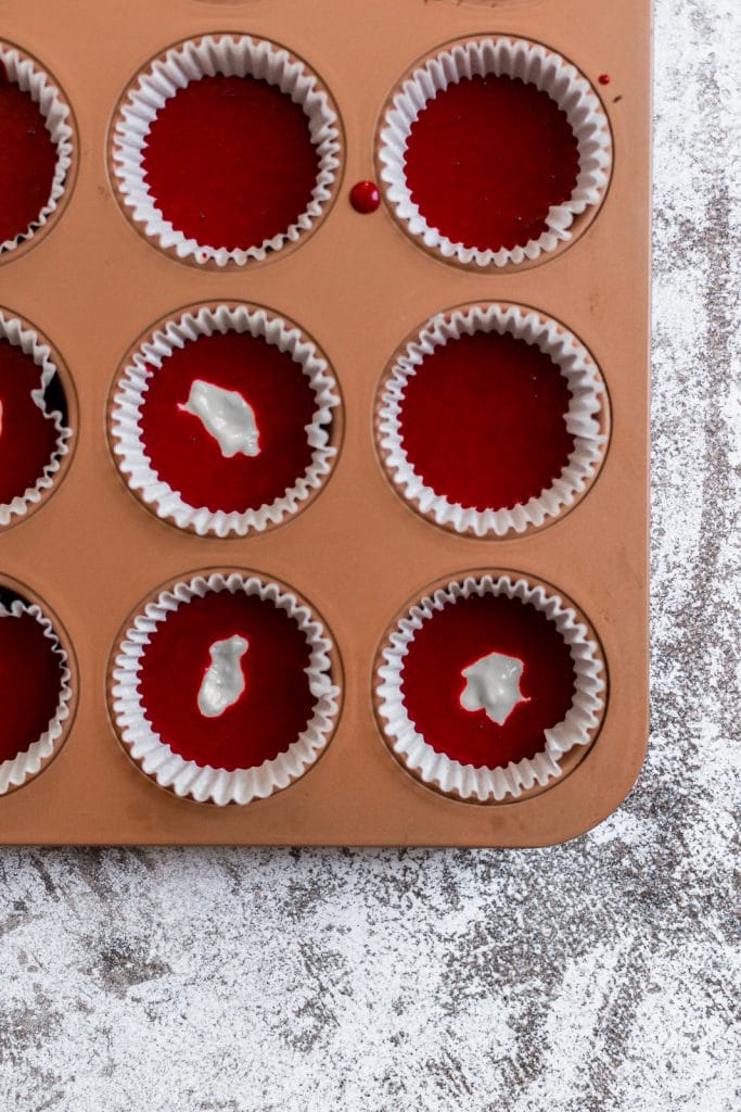 An orange cupcake tin lined with cupcake liners and filled with red velvet cupcake batter