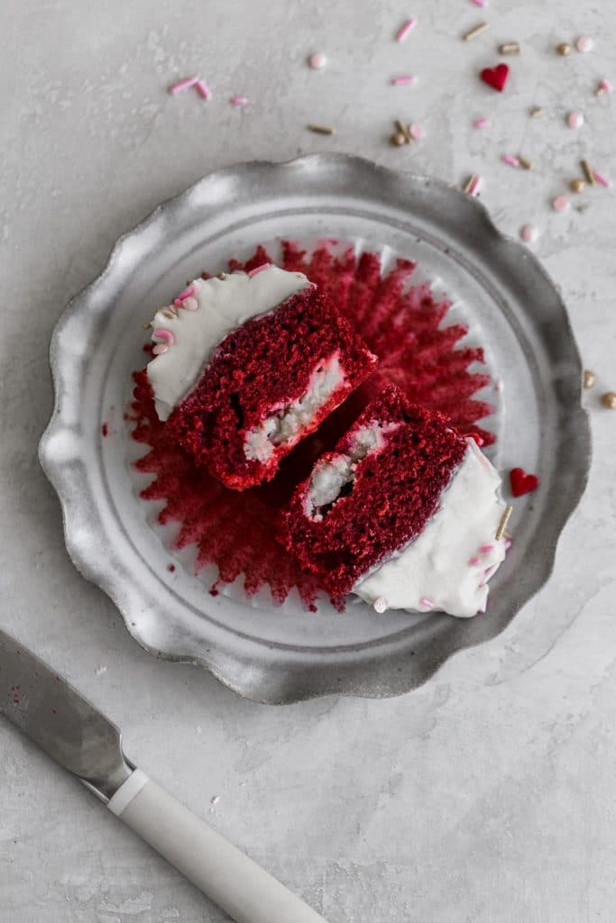 a red velvet cupcake cut in half to show the cheesecake filling inside set on a gray plate