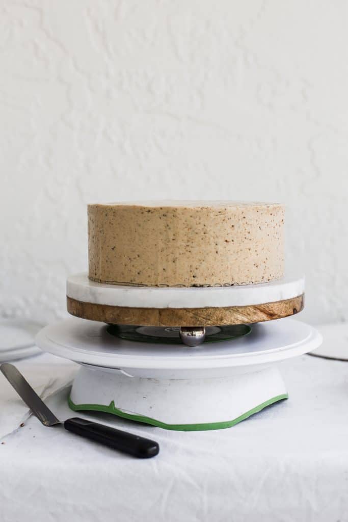 a beige cake sitting on a white and brown cake stand 