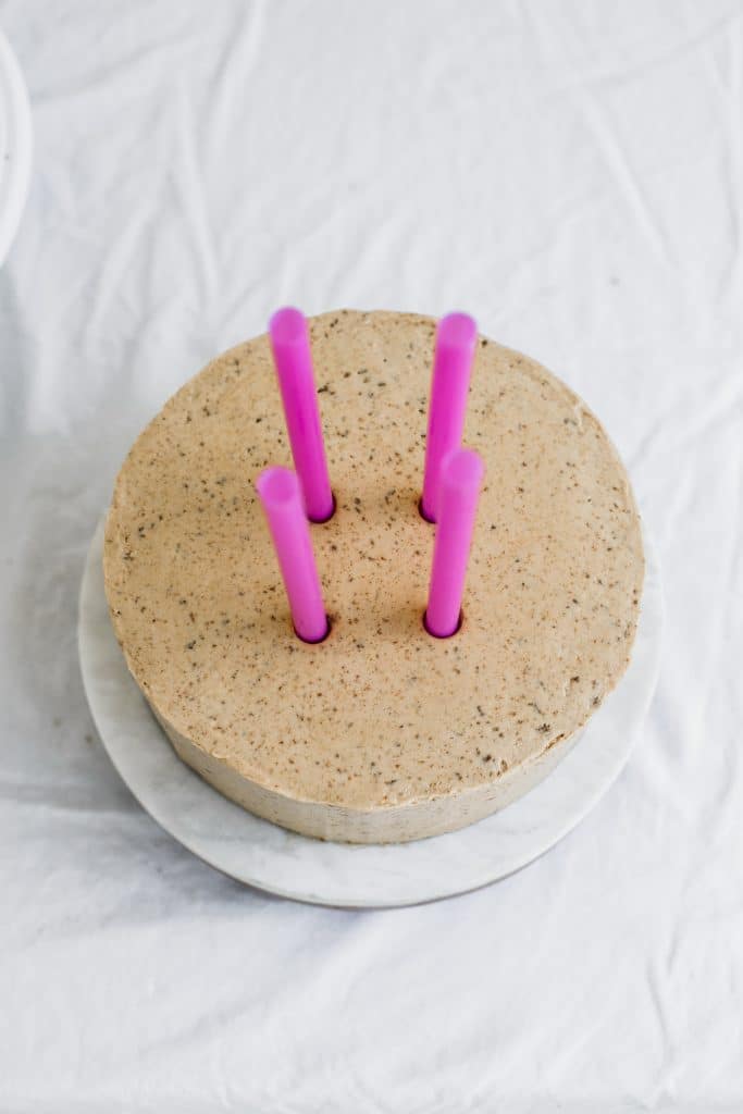 4 pink straws being insterted into the middle of a beige cake 