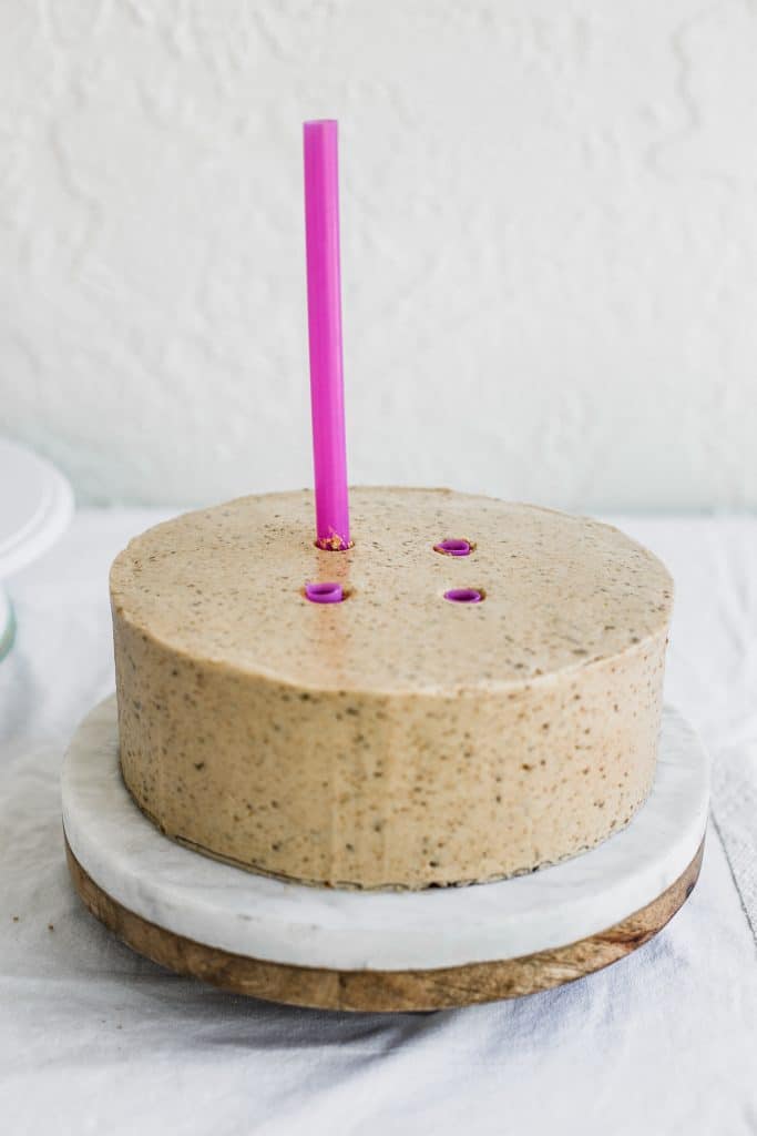 A pink straw being inserted in the middle of a  beige cake 