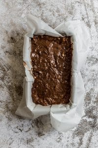 chocolate banana cake batter in a loaf pan lined with parchment paper