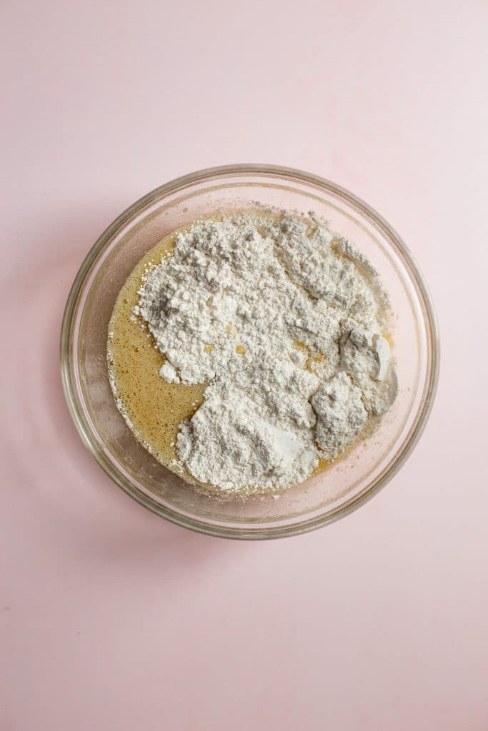 Flour added to a bowl of banana bread batter on a pink background