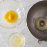 A mixing bowl with one egg white in it next to a small glass bowl with about egg white in it next to another glass bowl with egg yolks
