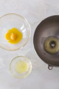 A mixing bowl with one egg white in it next to a small glass bowl with about egg white in it next to another glass bowl with egg yolks