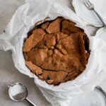 The cracked top of a chocolate cake in a springform pan lined with parchment paper.