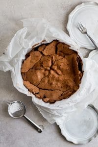 The cracked top of a chocolate cake in a springform pan lined with parchment paper.