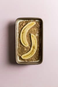 Banana bread batter in a loaf pan with a sliced banana on top