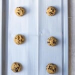 6 cookie dough balls on a parchment lined cookie sheet.