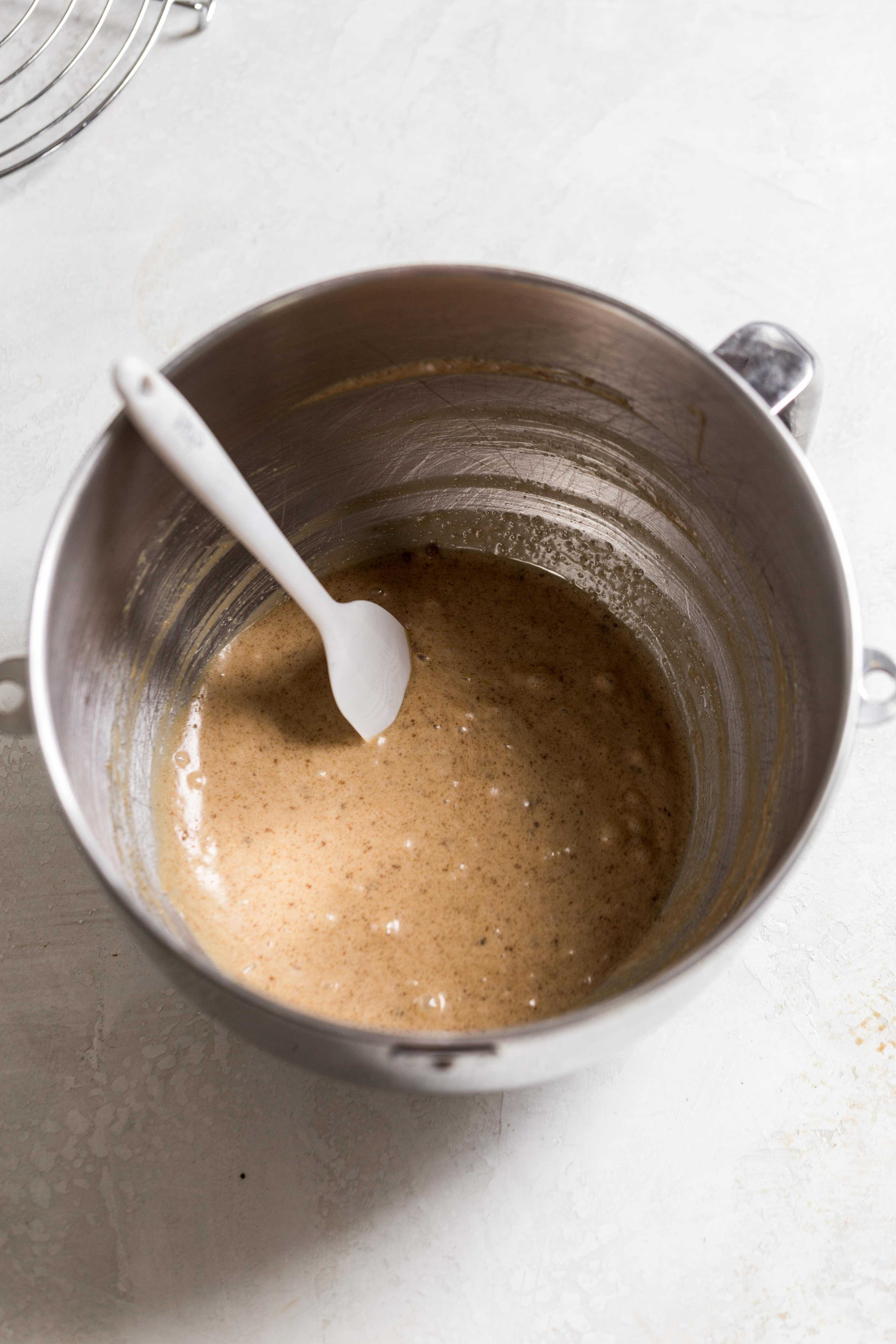 Brown cookie batter on the bottom of a mixing bowl on a gray surface.