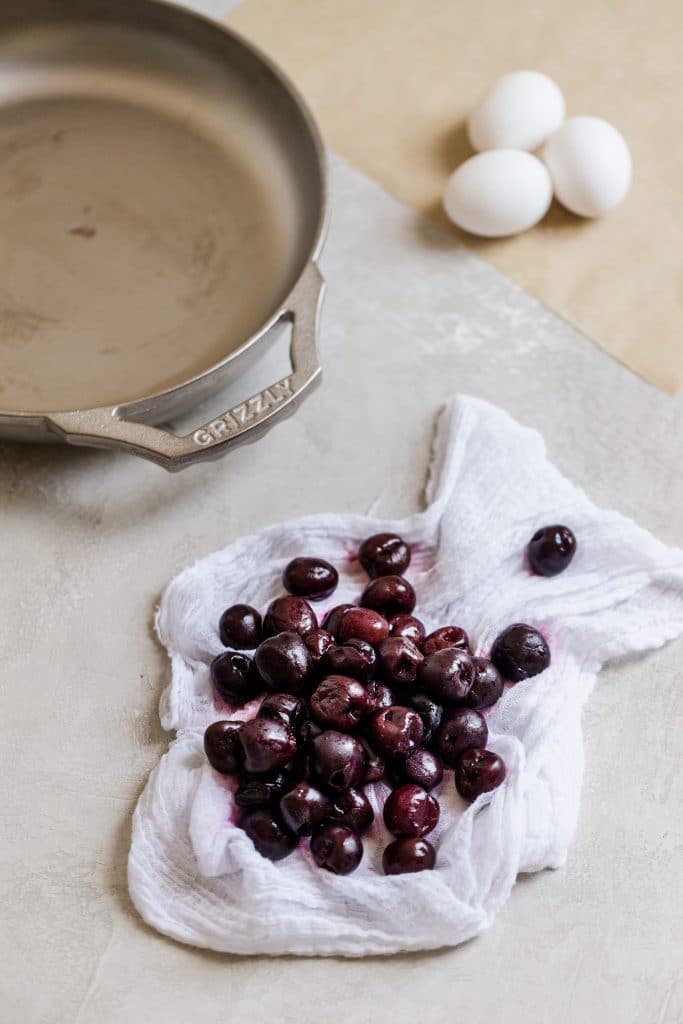 Frozen thawed cherries drying on a white cheesecloth on a grey background.