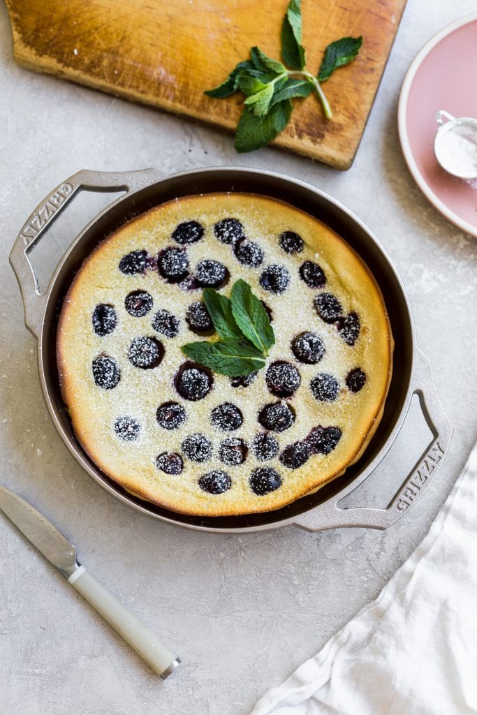 A cherry clafoutis made in a GRIZZLY nickel plated cast iron pan on a gray background.
