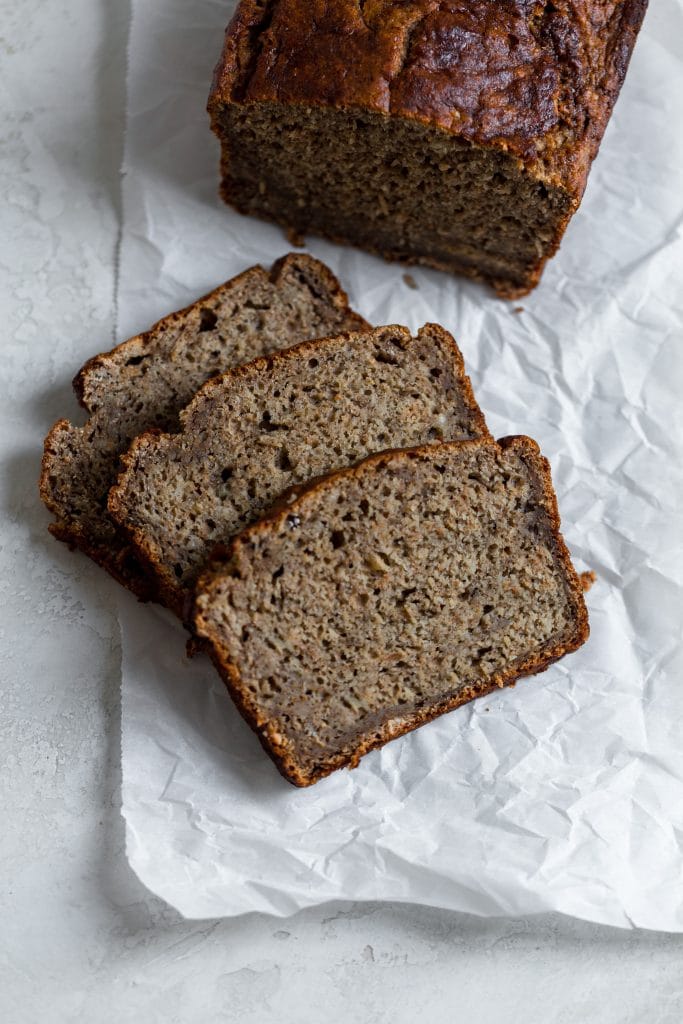 Three slices of banana bread laying on parchment paper on a gray background