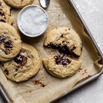 A chocolate chip cookie broken apart on a parchment paper lined cookie sheet with chocolate melting out of the middle/