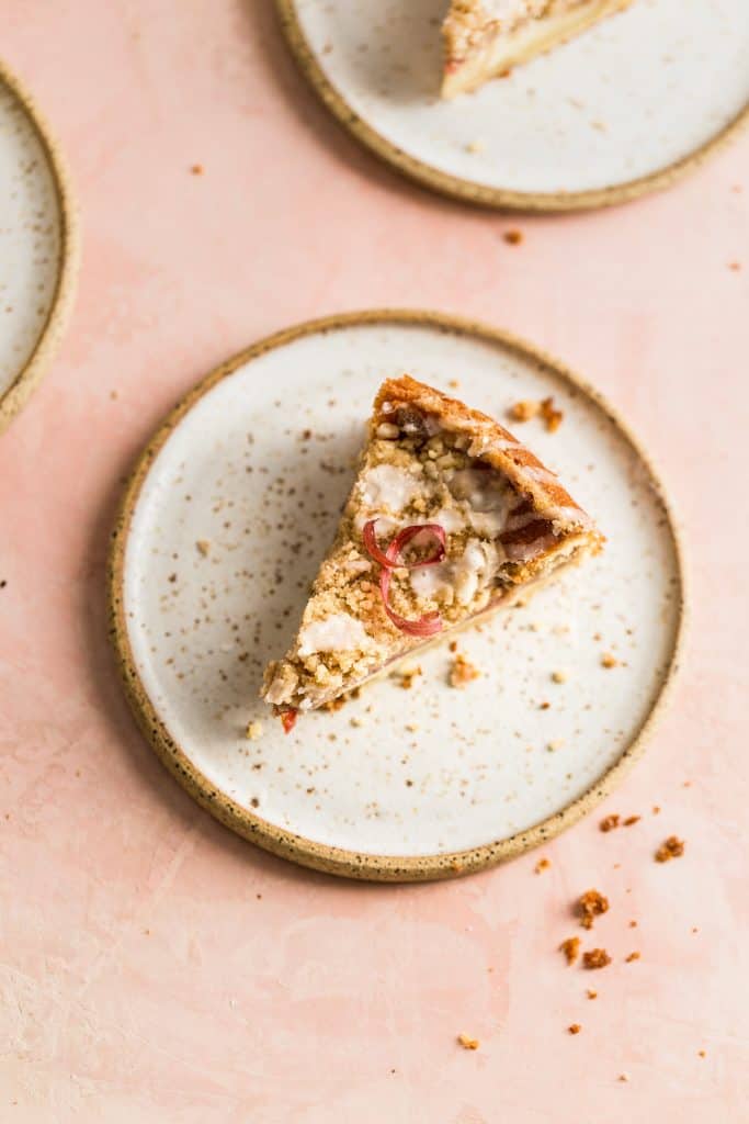 A slice of rhubarb coffee cake on a white speckled plate on a pink surface