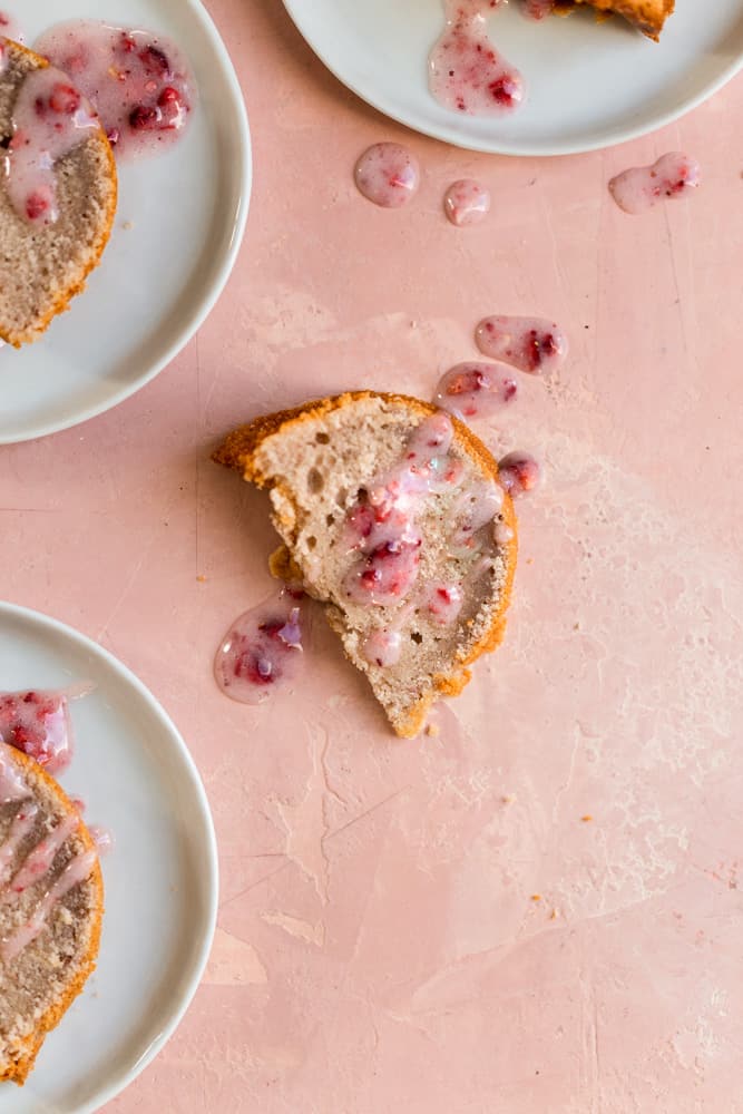 A slice of bundt cake drizzled with pink glaze on a pink surface