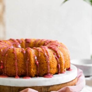Pink strawberry glaze dripping down a bundt cake next to a white surface