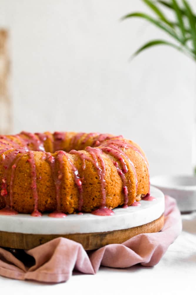 Pink strawberry glaze dripping down a bundt cake next to a white surface