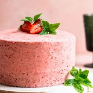 A pink frosted cake with strawberries and basil on top
