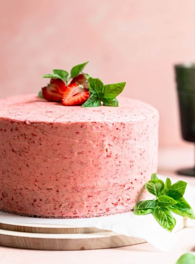 A pink frosted cake with strawberries and basil on top
