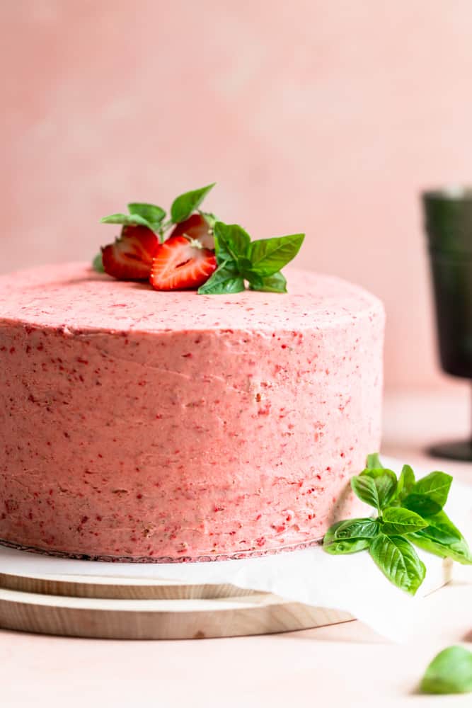 A pink frosted cake with strawberries and basil on top