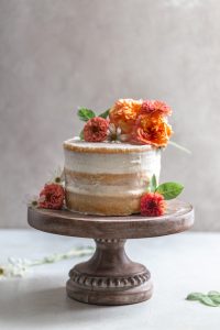 A naked cake with flowers on a wooden cake stand.