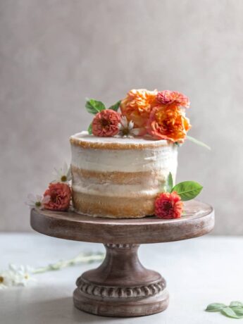 A naked cake with flowers on a wooden cake stand.