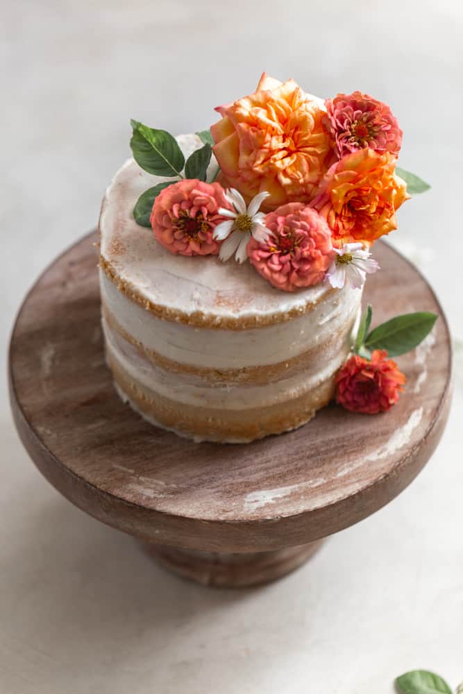 A cake topped with flowers on a wood cake stand.