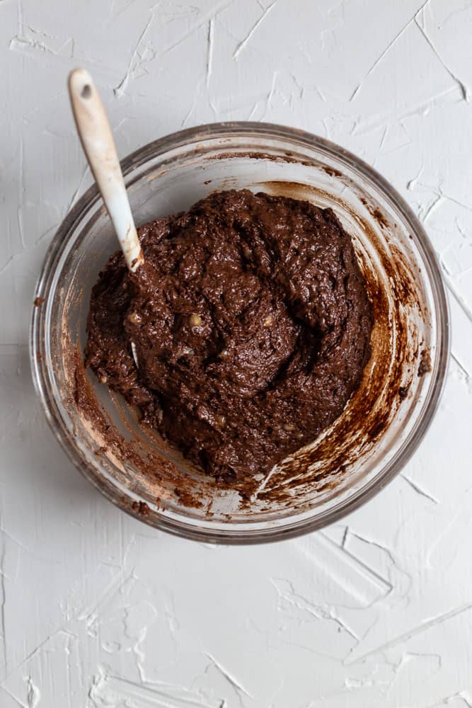 Thick chocolate muffin batter in a glass bowl on a light gray background.