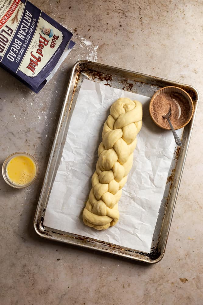 a 6 strand braided challah on a piece of parchment paper on a sheet tray