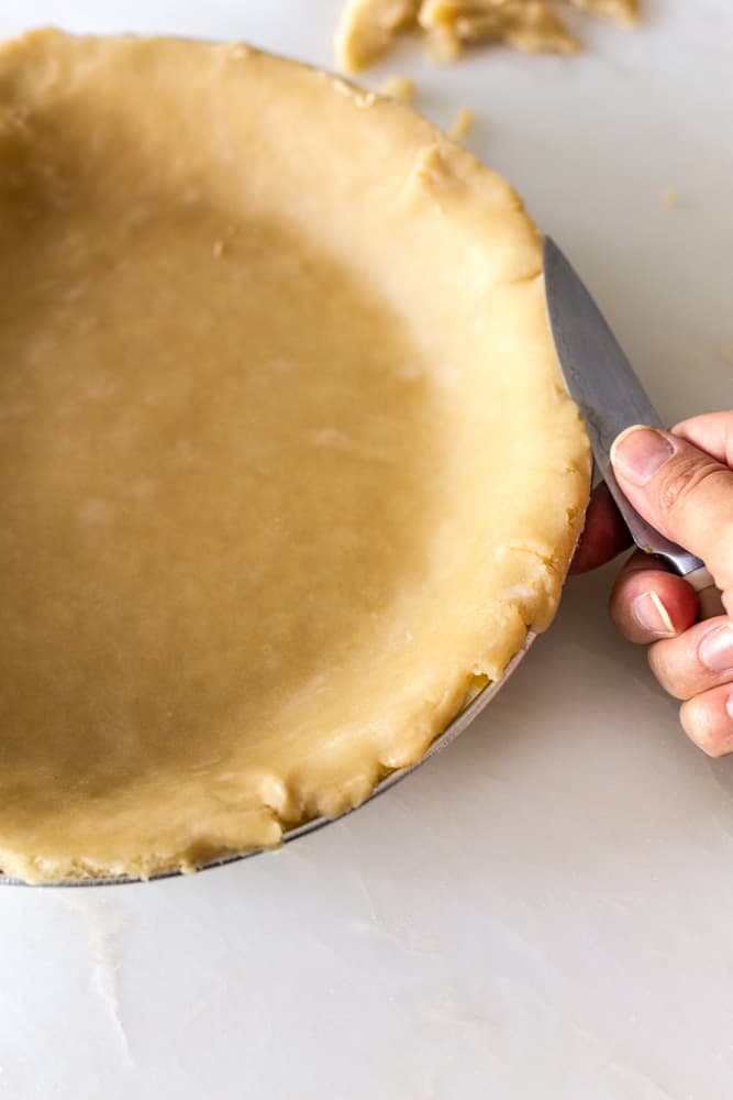 a knife trimming the edges of a flaky pie crust