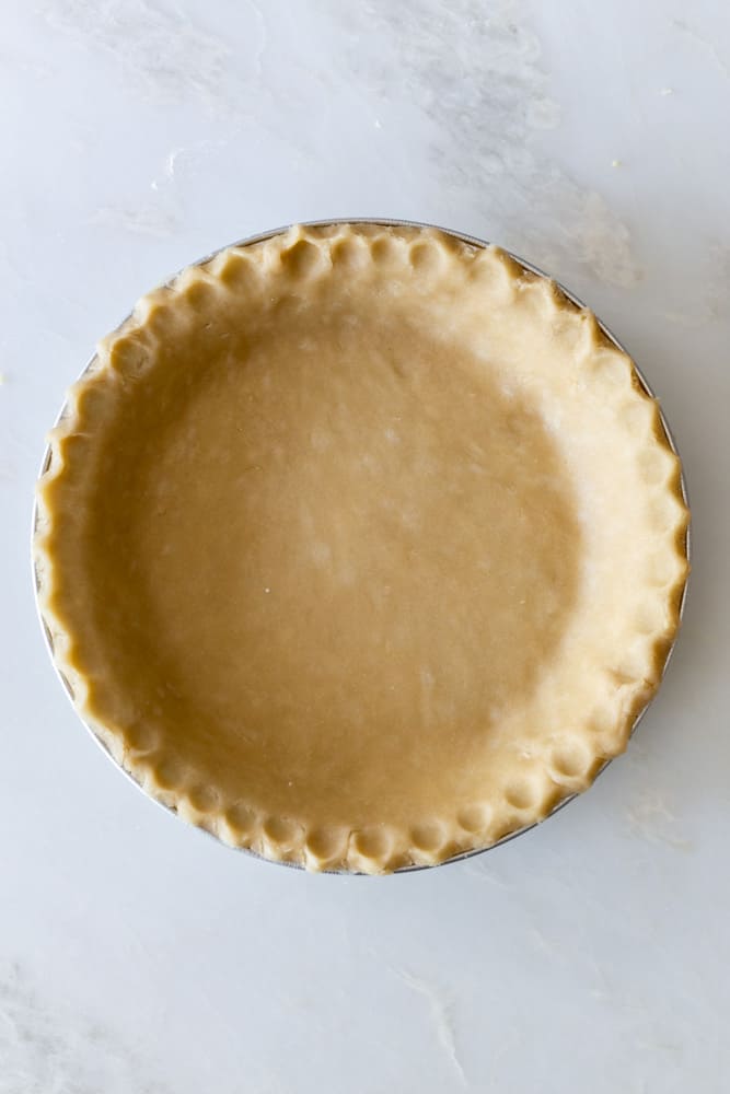 Unbaked pie crust with crimped edges on a white surface