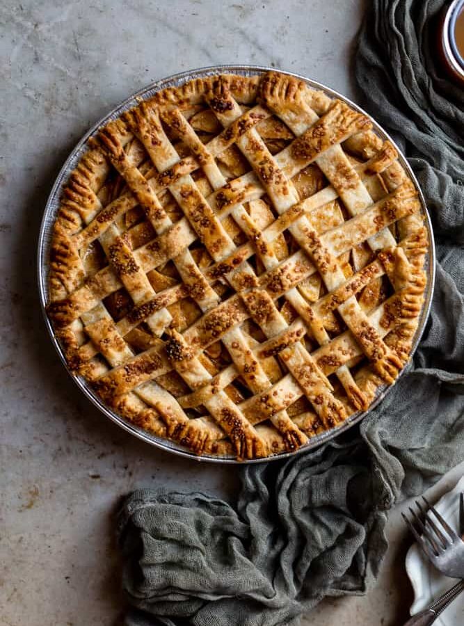 A lattice topped apple pie next to a green gauze napkin on a textured surface