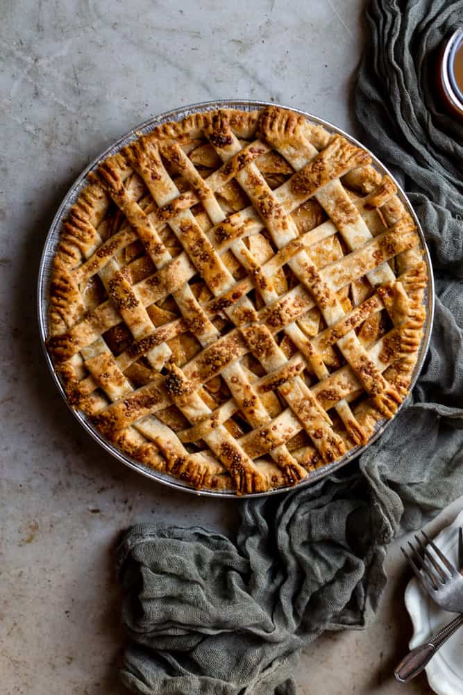 A lattice topped apple pie next to a green gauze napkin on a textured surface