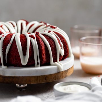 A thick cream cheese frosting drizzled on a bundt cake with pink cups in the background