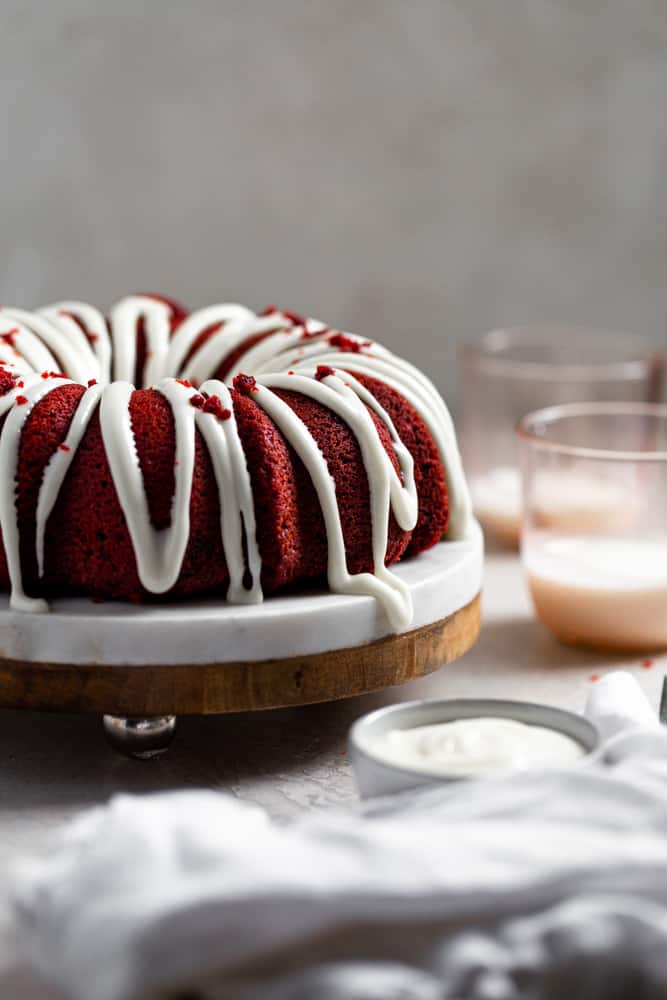 A thick cream cheese frosting  drizzled on a bundt cake with pink cups in the background