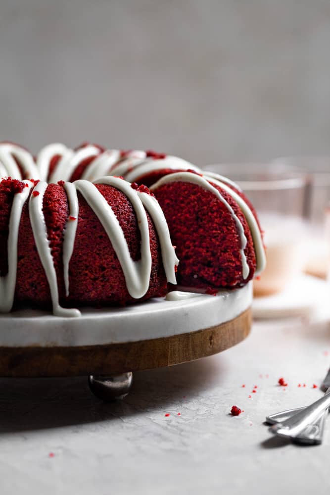 A slice of cake sliced away from the rest of the red velvet bundt cake on a cake stand 