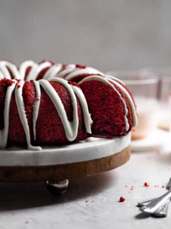 A slice of cake sliced away from the rest of the red velvet bundt cake on a cake stand