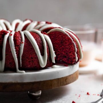 A slice of cake sliced away from the rest of the red velvet bundt cake on a cake stand