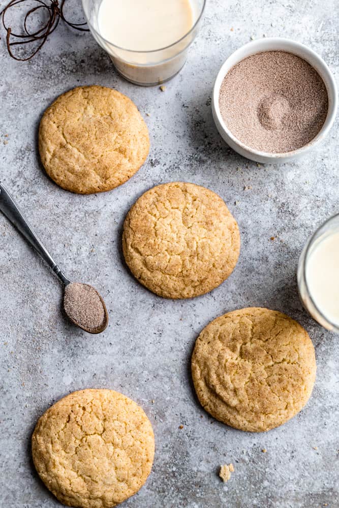 Eggnog snickerdoodle cookies on a textured background next to a bowl of cinnamon sugar