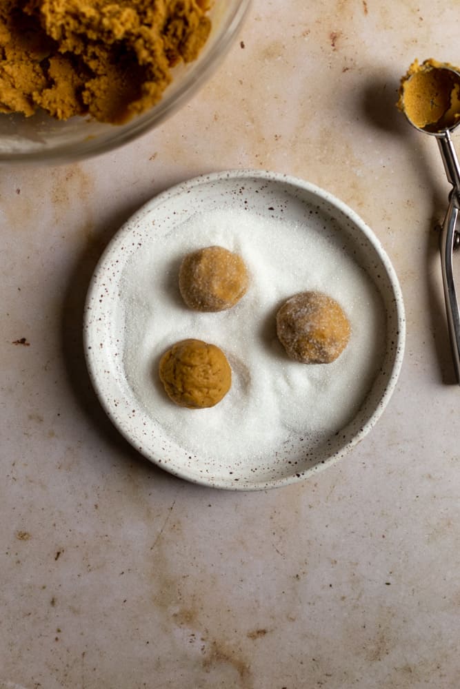 three cookie dough balls rolling in sugar in a bowl