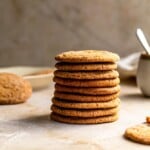 Gingersnaps stacked on each other with a mug in the background on a tan surface